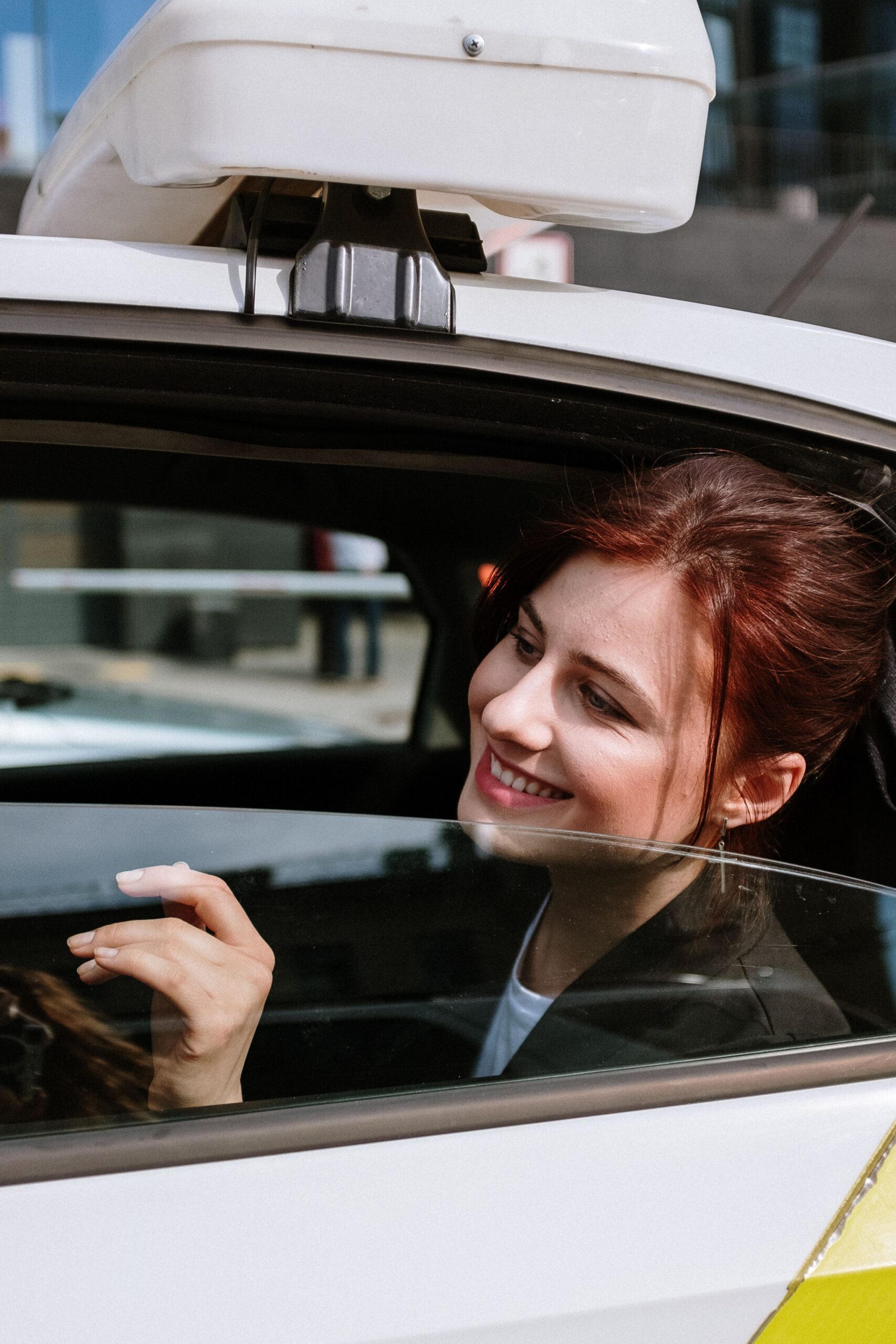Smiling passenger in the back seat of a white car with an unbranded rooftop light box (reads slightly taxi rather than U