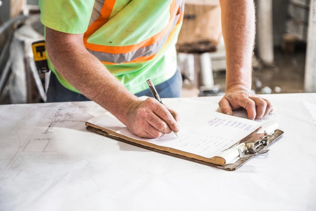Worker in hi-vis vest filling out paperwork on a clipboard over site plans