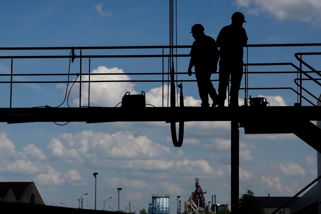 Silhouettes of two hard-hat workers on an elevated industrial walkway
