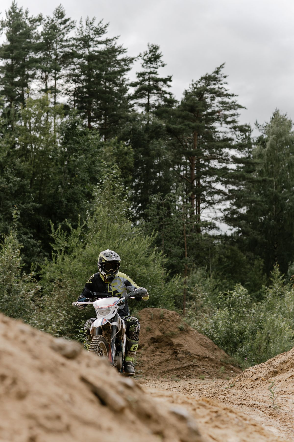 Rider on a dirt bike navigating an actual off-road dirt trail through a forest, no brand logos visible