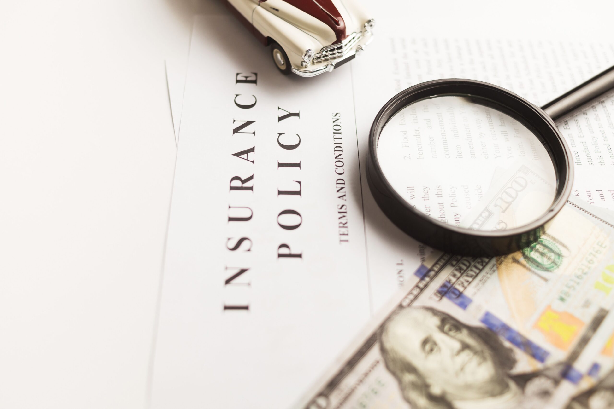 Insurance policy document (generic, no insurer branding) with toy car, magnifying glass, and cash &mdash; auto-insurance-claim
