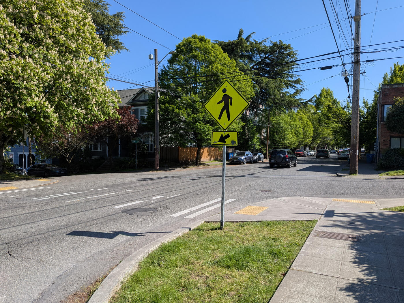 A yellow pedestrian-crossing warning sign beside a quiet residential street crosswalk