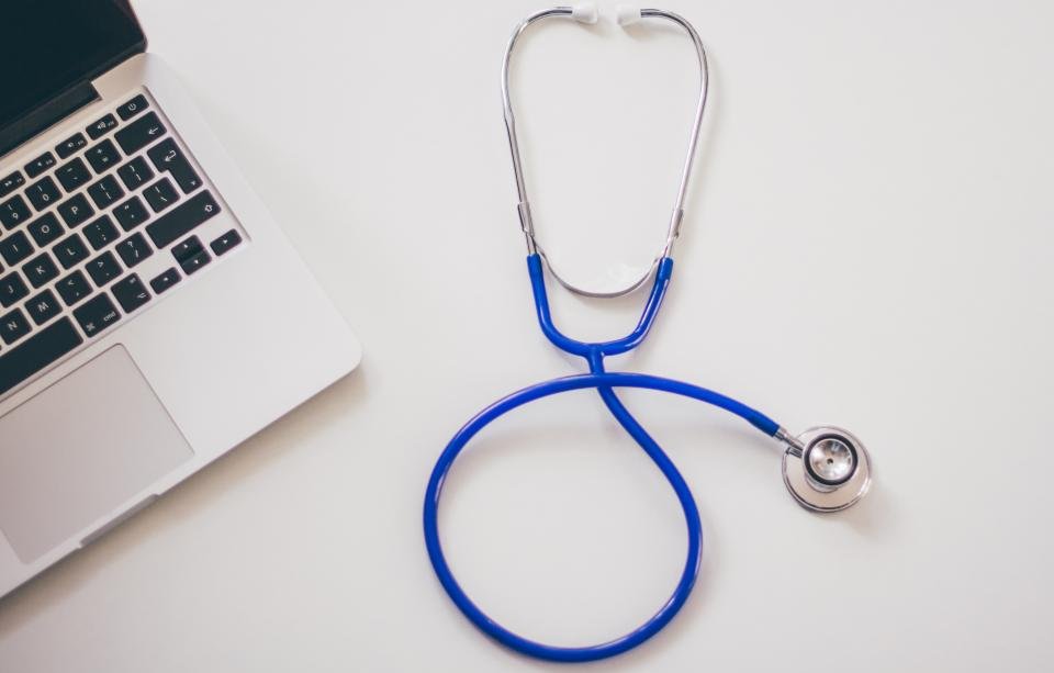 Stethoscope resting beside a laptop on a desk